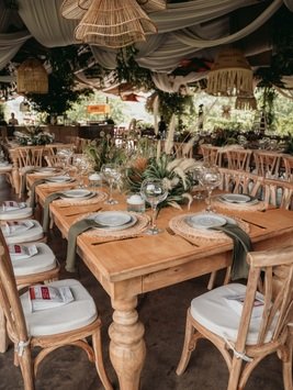 Mesa imperial de madera con vajilla y centros de mesa verdes bajo lámparas de mimbre